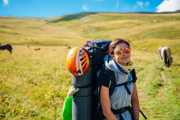Menina com uma mochila grande e um capacete com óculos no campo — Fotografia de Stock