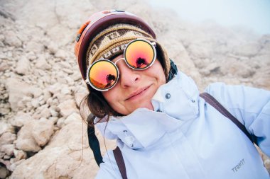 Güneş gözlüklü turist kız, dağların arka planında selfie çekiyor.