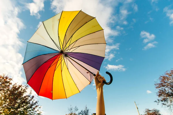 Jovem mulher de pé com um guarda-chuva multi-colorido e gira-lo contra com um céu azul — Fotografia de Stock