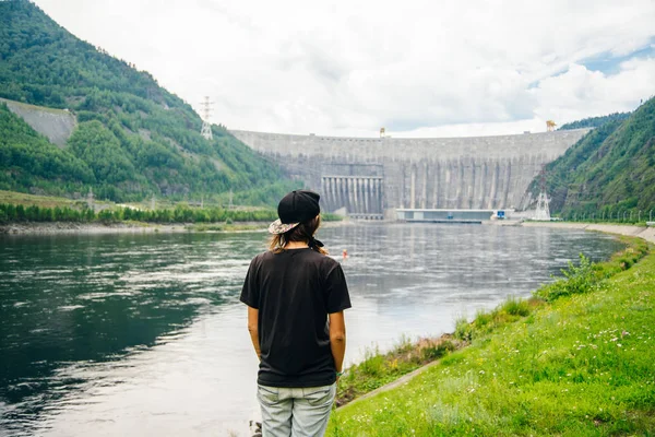 Dziewczyna patrzy na elektrownię wodną nad rzeką Yenisei na Syberii. Zapora Sayano-Shushenskaya — Zdjęcie stockowe