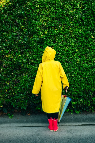 Menina em uma capa de chuva amarela em um fundo de uma parede com grama — Fotografia de Stock