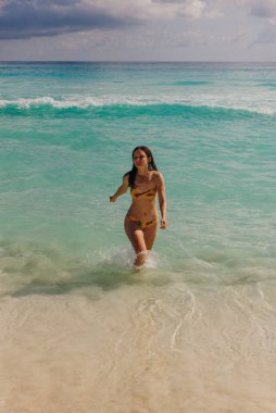 Parlak mayo giymiş esmer kız Cancun, Meksika sahilinde koşuyor.