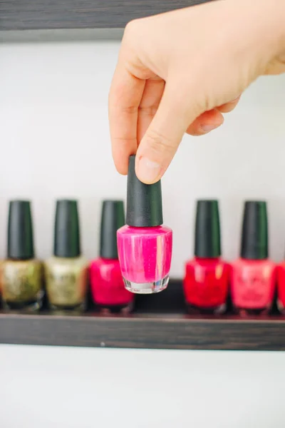 girl holds nail polish on the background of nail polishes