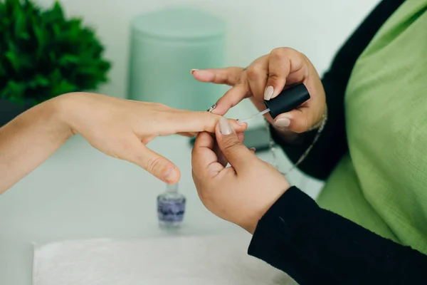 Manicurist applying cuticle softener or clear nail varnish to the fingernails of a lady client in a spa or beauty salon