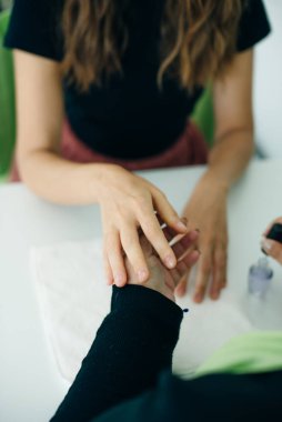 Manikürcü ya da manikürcü, kaplıcadaki ya da güzellik salonundaki bir bayanın tırnaklarına oje sürüyor.