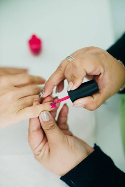 Manikürcü, spa ya da güzellik salonundaki bir bayanın tırnaklarına pembe oje sürüyor.