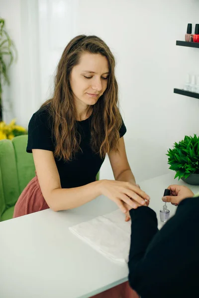 Manicurista aplicando suavizante de cutículas o barniz de uñas claro a las uñas de una clienta en un spa o salón de belleza — Foto de Stock
