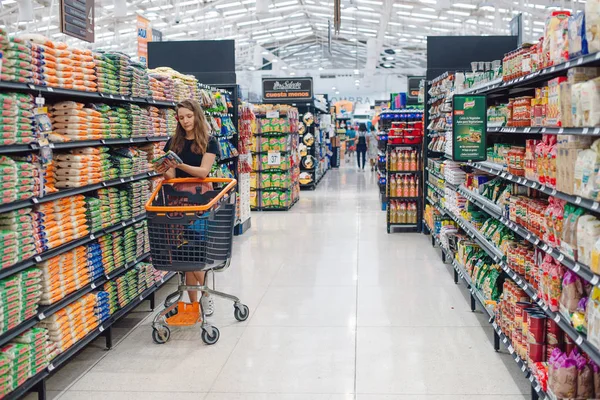 Image of pretty woman with cart choosing products in supermarket — Stock Photo, Image