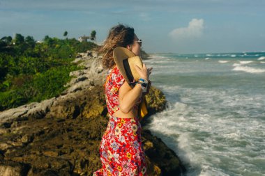Şapkalı ve siyah elbiseli güzel bir kız okyanusa bakıyor. TULUM, Meksika