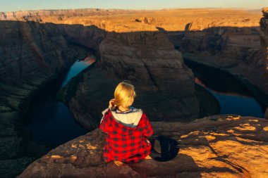 Sarışın kız, Glen Canyon Ulusal Eğlence Bölgesi 'nde sabah erkenden at nalı bükme yerinde oturuyor.