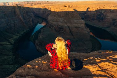 Sarışın kız, Glen Canyon Ulusal Eğlence Bölgesi 'nde sabah erkenden at nalı bükme yerinde oturuyor.