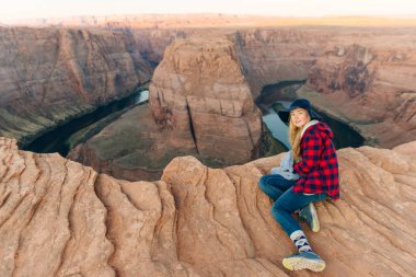 Sarışın kız, Glen Canyon Ulusal Eğlence Bölgesi 'nde sabah erkenden at nalı bükme yerinde oturuyor.