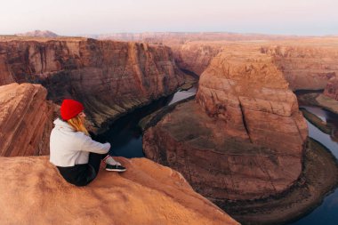 Sarışın kız, Glen Canyon Ulusal Eğlence Bölgesi 'nde sabah erkenden at nalı bükme yerinde oturuyor.