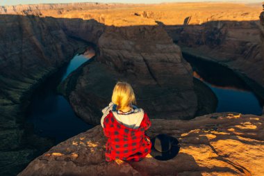 Sarışın kız, Glen Canyon Ulusal Eğlence Bölgesi 'nde sabah erkenden at nalı bükme yerinde oturuyor.