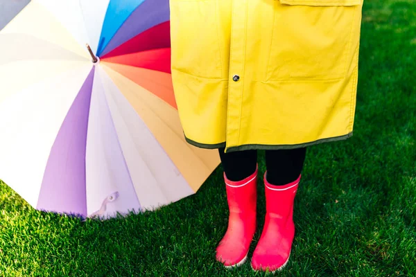 Żółty płaszcz przeciwdeszczowy. Gumowe różowe buty przeciwko. Koncepcyjny wizerunek nóg w butach na zielonej trawie. parasol — Zdjęcie stockowe