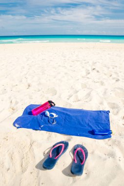 tatil ve yaz tatili konsepti - parmak arası terlikler, havlu, şişe su ve kumsalda bir şişe güneş kremi yağı