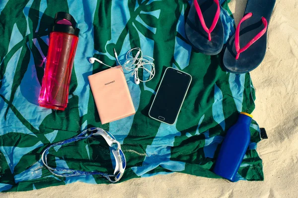 Concepto de vacaciones y vacaciones de verano - chanclas, toalla, gorra, agua embotellada y botella de aceite protector solar en la arena de la playa —  Fotos de Stock