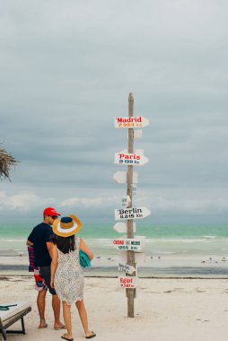 Ada Holbox, Meksika - Şubat 2020 Plajda genç gezginler yakındaki şehirler ve yerel yemekleri gösteren bir tabela ile.