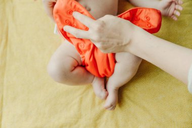 Annenin ellerini kapat. Yeni doğan bebeğine turuncu bir bebek bezi tak.