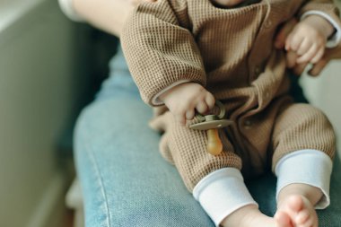 Bebek annesinin kollarında bir emzik tutuyor..