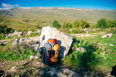 Sırt çantası, güneşli bir günde ufka uzanan dağların arka planında duruyor....