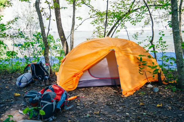 Orange camping tent with backpack in the cozy green forest