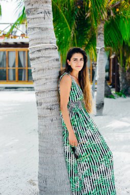 Güneş gözlüklü güzel bir kız, beyaz bir sahilde parlak bir elbise içinde..