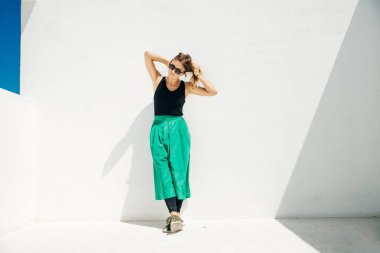 Uzun yeşil etekli bir kız güneşli bir günde beyaz bir duvara karşı.