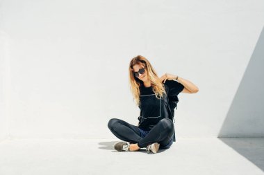 Güneş gözlüklü ve siyah giyen, beyaz arka planda sırt çantalı bir kız..