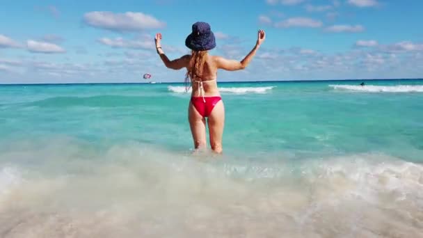 Widok na tył kobiety w stroju kąpielowym z blond długimi włosami i kapeluszem stojącej na tropikalnej plaży. 4k. Meksyk, Cancun — Wideo stockowe