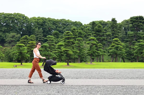 Onun küçük bebek Bebek arabasını rahatlatıcı ile Tokyo İmparatorluk Sarayı bahçeleri zevk genç bir anne — Stok fotoğraf