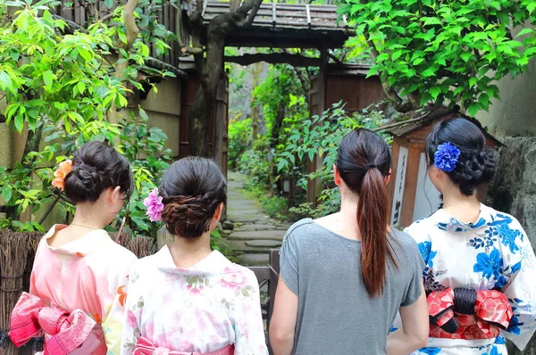 Three Japanese young woman wearing summer yukatas and an European female tourist walk together through a Japanese typical garden\'s entrance close to World Heritage Kiyomizu Temple in Kyoto, Japan