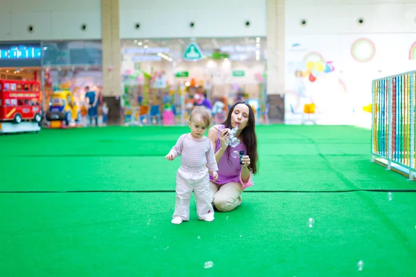 Moeder en baby blazen van zeepbellen op de children's center — Stockfoto