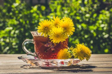 Bahar güneşli yeşil bahçe, parlak sarı karahindibalar ve bir fincan sıcak bitki çayı.