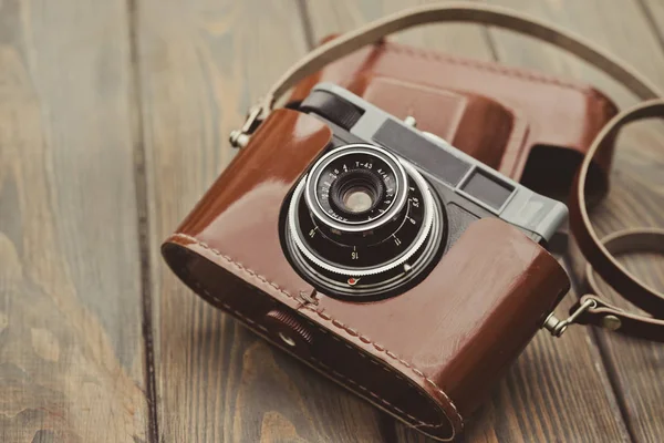 Old film camera in a brown leather case against the background of a wooden table