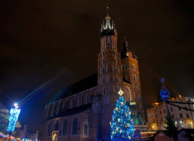 Krakow / Polonya - 29 Kasım 2019: Katolik Mariacki Kilisesi ve Krakow, Polonya 'daki eski Pazar Meydanı' ndaki ortaçağ pazarı kumaşı sıraları. Noel arifesinde bir gece eski Avrupa şehri