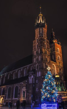 Krakow / Polonya - 29 Kasım 2019: Katolik Mariacki Kilisesi ve Krakow, Polonya 'daki eski Pazar Meydanı' ndaki ortaçağ pazarı kumaşı sıraları. Noel arifesinde bir gece eski Avrupa şehri