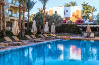 Sharm el Sheikh, Mısır - 03 Aralık 2019: Sharm El Sheikh, Sina Yarımadası, Mısır 'da lüks bir tropikal tatil köyünde temiz bir yüzme havuzu ve güverte sandalyeleri. Modern turistik binalar ve palmiye ağaçları. Orta Doğu 'da Tatiller