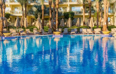 Sharm el Sheikh, Mısır - 03 Aralık 2019: Sharm El Sheikh, Sina Yarımadası, Mısır 'da lüks bir tropikal tatil köyünde temiz bir yüzme havuzu ve güverte sandalyeleri. Modern turistik binalar ve palmiye ağaçları. Orta Doğu 'da Tatiller