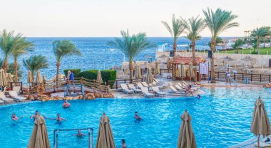 Sharm el Sheikh, Mısır - 03 Aralık 2019: Sharm El Sheikh, Sina Yarımadası, Mısır 'da lüks bir tropikal tatil köyünde temiz bir yüzme havuzu ve güverte sandalyeleri. Modern turistik binalar ve palmiye ağaçları. Orta Doğu 'da Tatiller
