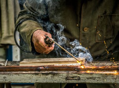 Eski köy kaynak atölyesi. Metal ve kaynak elektrotlarıyla çalışan yaşlı bir adam.