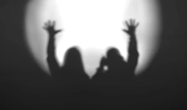 Black and white couple silhouettes with hands up in light of floodlight backdrop