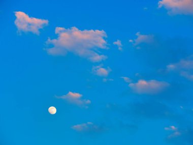 Mavi gökyüzünde parlayan ay ve bulutlar.