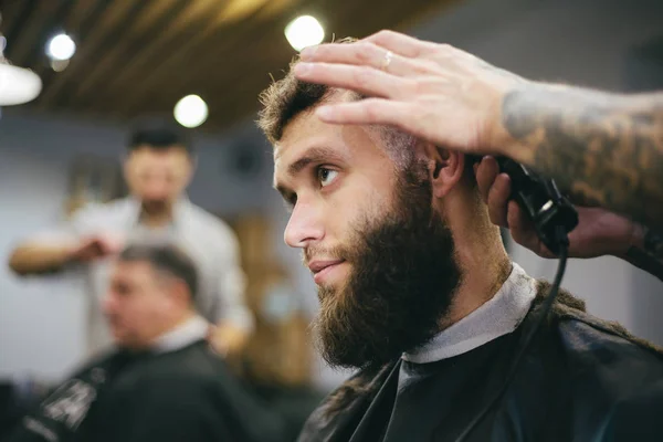 Homem barbudo cortando cabelo e barba no barbeiro local — Fotografia de Stock