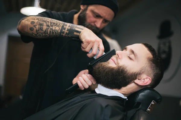 Бородач стрижёт волосы и бороду у местного парикмахера — стоковое фото