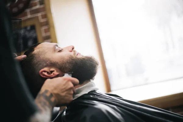 Homem barbudo cortando cabelo e barba no barbeiro local — Fotografia de Stock