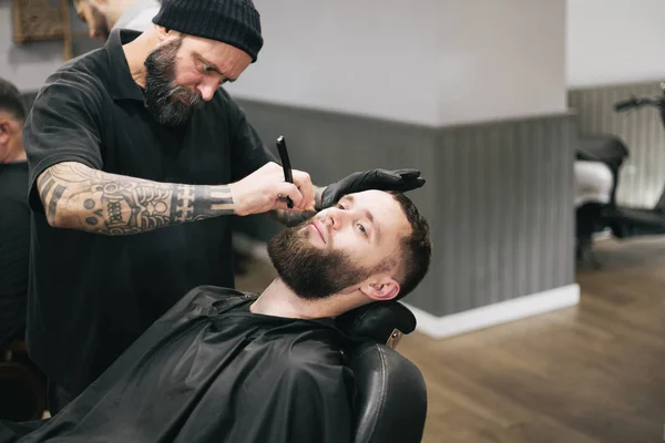 Бородач стрижёт волосы и бороду у местного парикмахера — стоковое фото