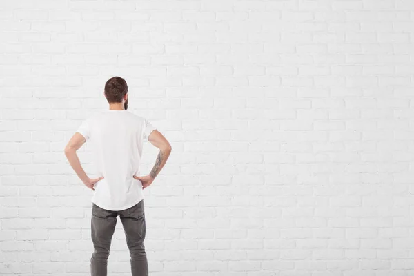 Uomo guardando invecchiato vernice bianco mattone muro di sfondo — Foto Stock