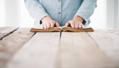 Ellerin ahşap masanın üzerinde İncil 'le dua ediyor.