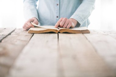 Ellerin ahşap masanın üzerinde İncil 'le dua ediyor.